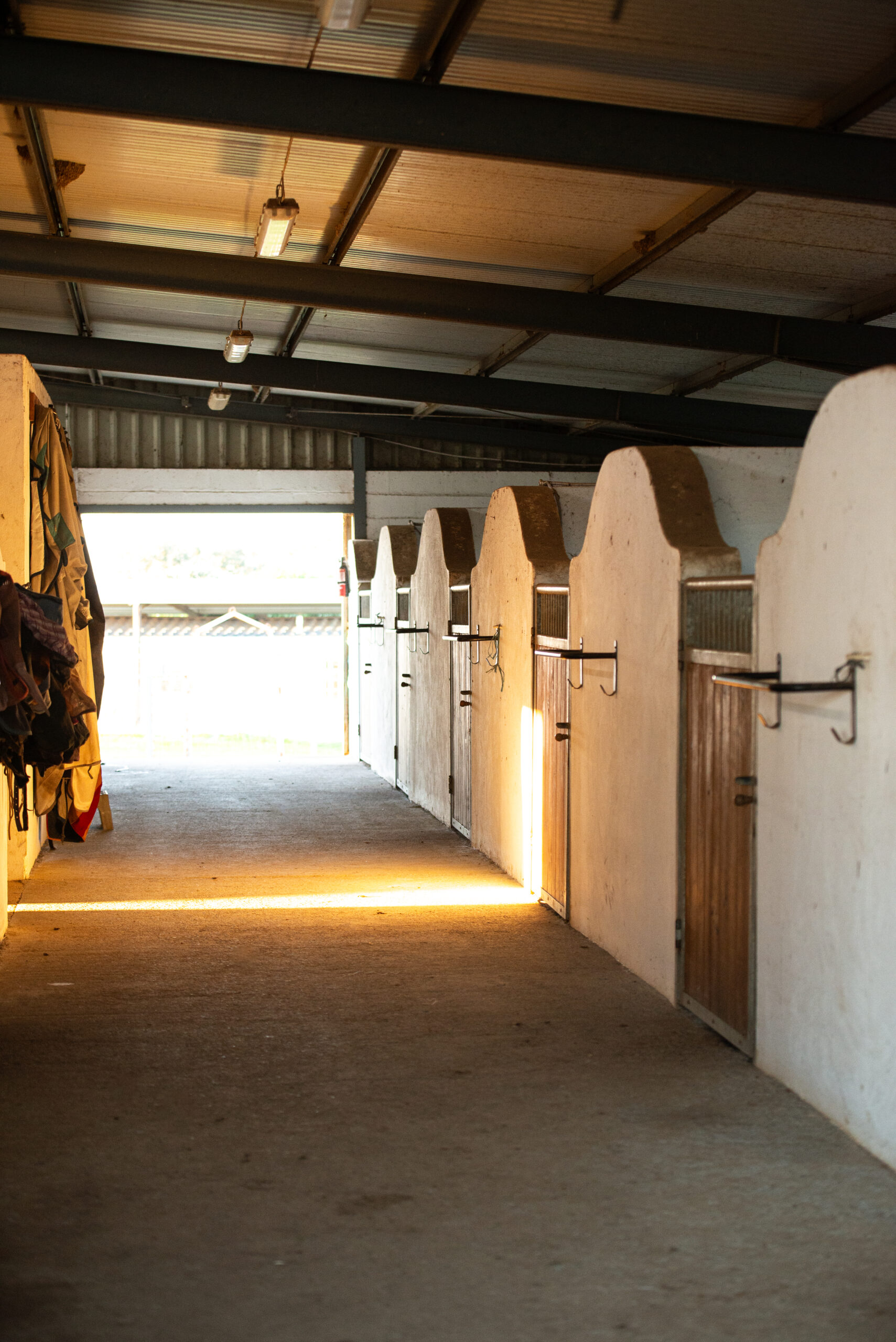 Stable alley with six horse boxes on the right in a brick built American barn in the evening light