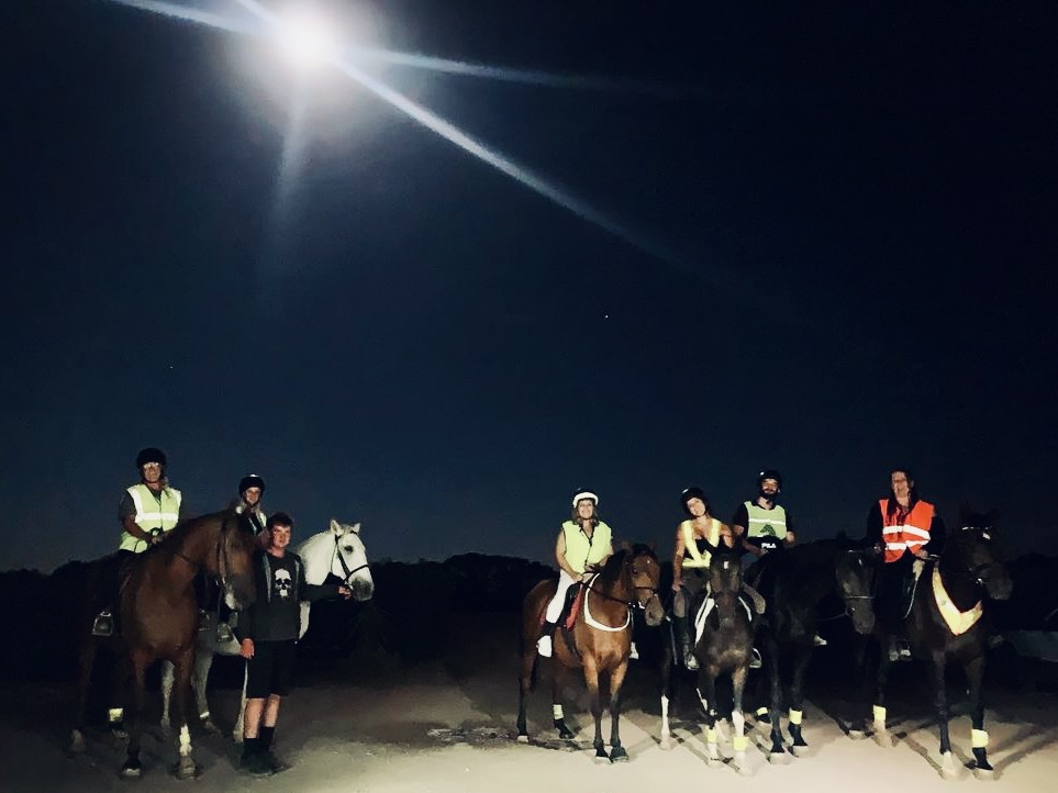 Six people on horses standing in front of a full moon sky