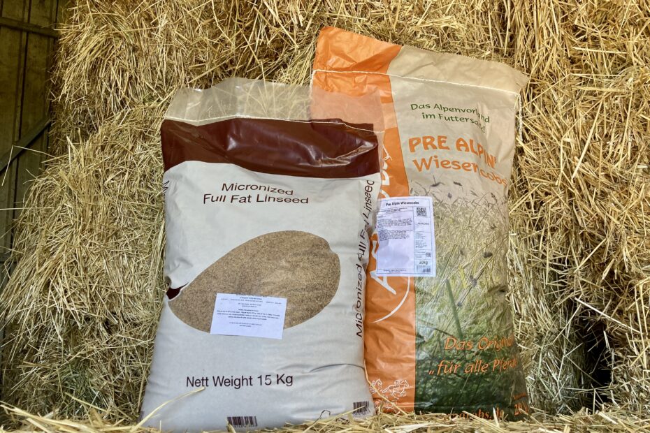 Product shot of one bag of EQ Micronized Full Fat Linseed together with one bag of Agrobs PreAlpin hay cobs arranged together on a bale of hay