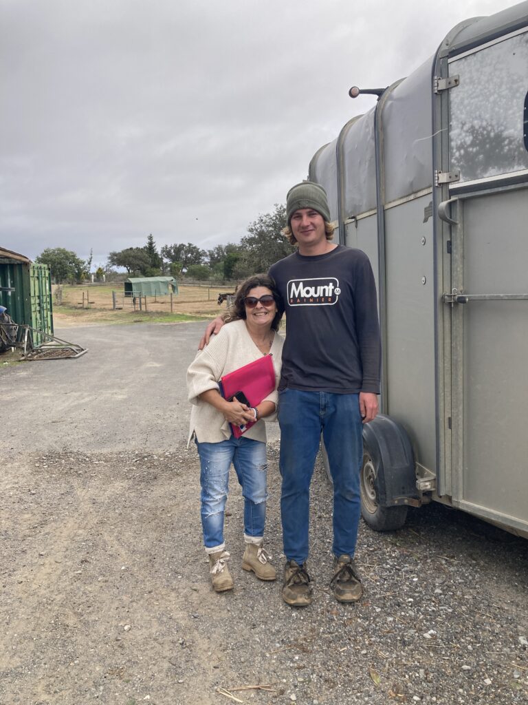 A small women and a tall man standing in front of a horse trailer